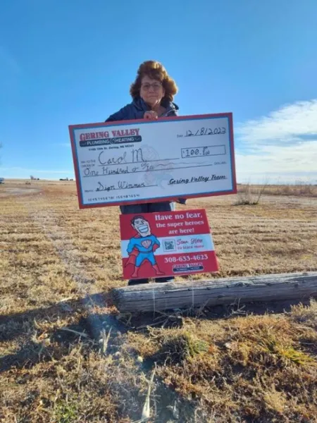 December yard-sign winner Carol M. with their Gering Valley Plumbing & Heating sign